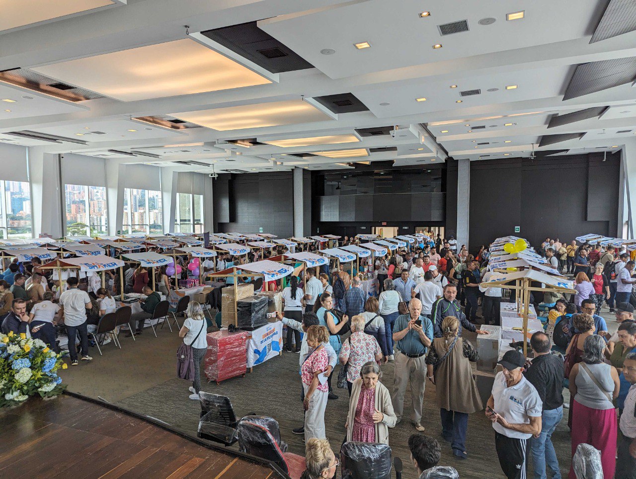 A revenda transfronteiriça de importações é um evento interior de grande escala em que um grande número de pessoas se levanta e conversa em torno de uma mesa com vários itens em exposição numa sala com grandes janelas e vistas para a cidade.